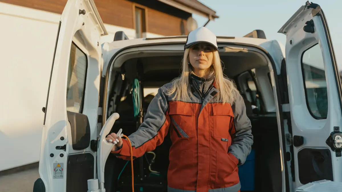 Trabajadora de limpieza con uniforme rojo junto a una camioneta de servicio con el equipo de limpieza