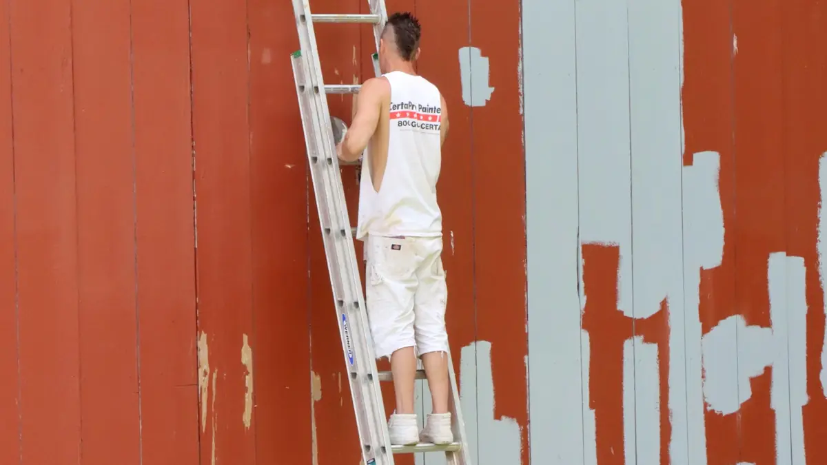 Pintor sobre una escalera repintando una pared exterior de madera